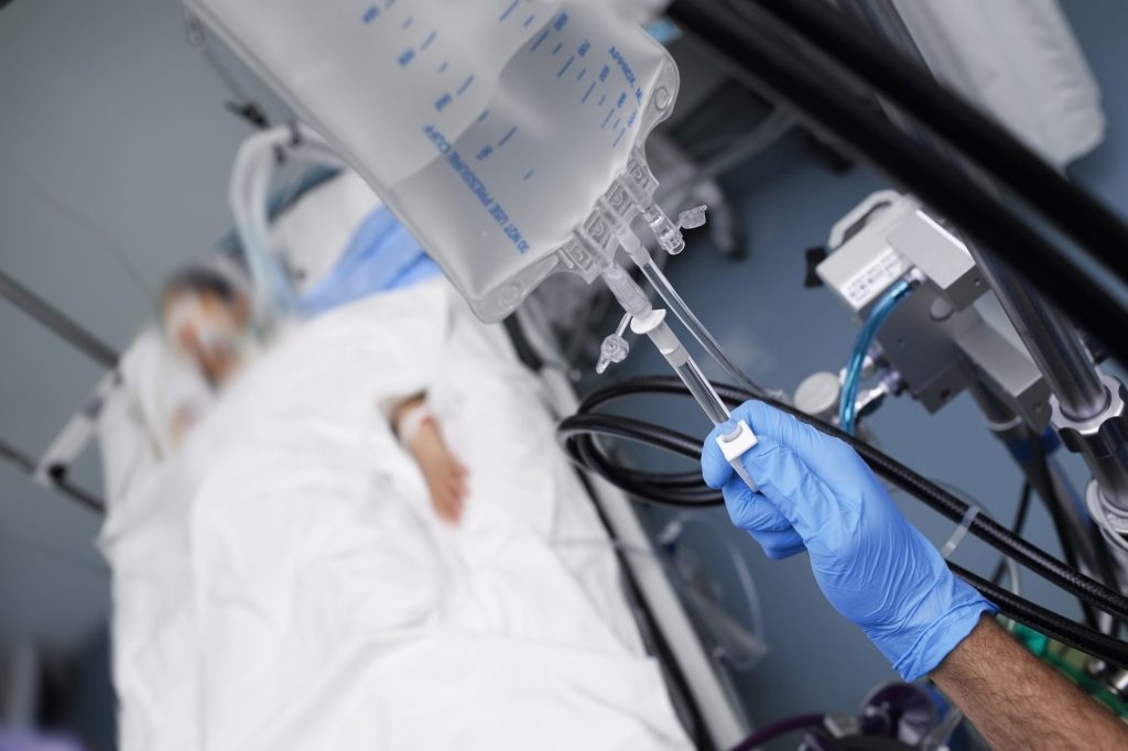 Male person with gloved hand turns off intravenous drug system in unconscious patient.