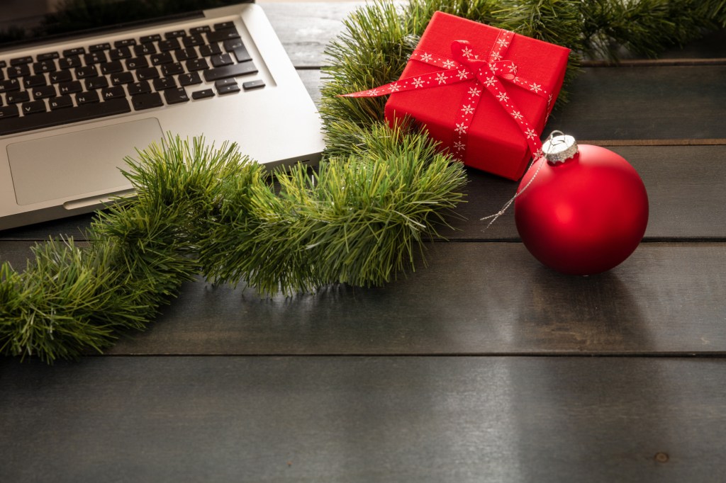 Laptop, gift box and Christmas wreath on a blue wooden table, signifying the office is closed for the holidays.